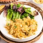 A plate of cheesy ritz cracker chicken casserole casserole topped with breadcrumbs, served with a side of mixed greens.