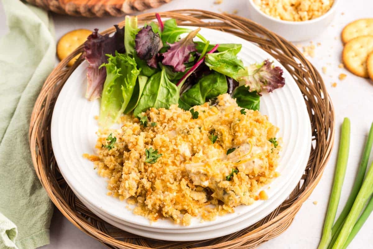 A plate of cheesy ritz cracker chicken casserole casserole topped with breadcrumbs, served with a side of mixed greens.