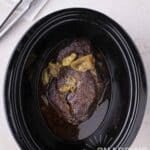 A pot roast cooked with pepperoncini peppers in a slow cooker.