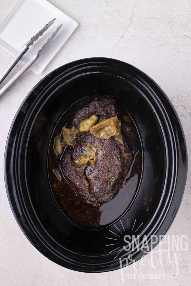 A pot roast cooked with pepperoncini peppers in a slow cooker.