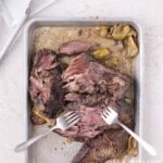 Shredded roast beef with peppers in a metal baking pan being pulled apart with two forks.