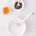 A bowl of creamy herb dressing with a fork, a small bowl of dried herbs with a spoon, and a glass of honey.