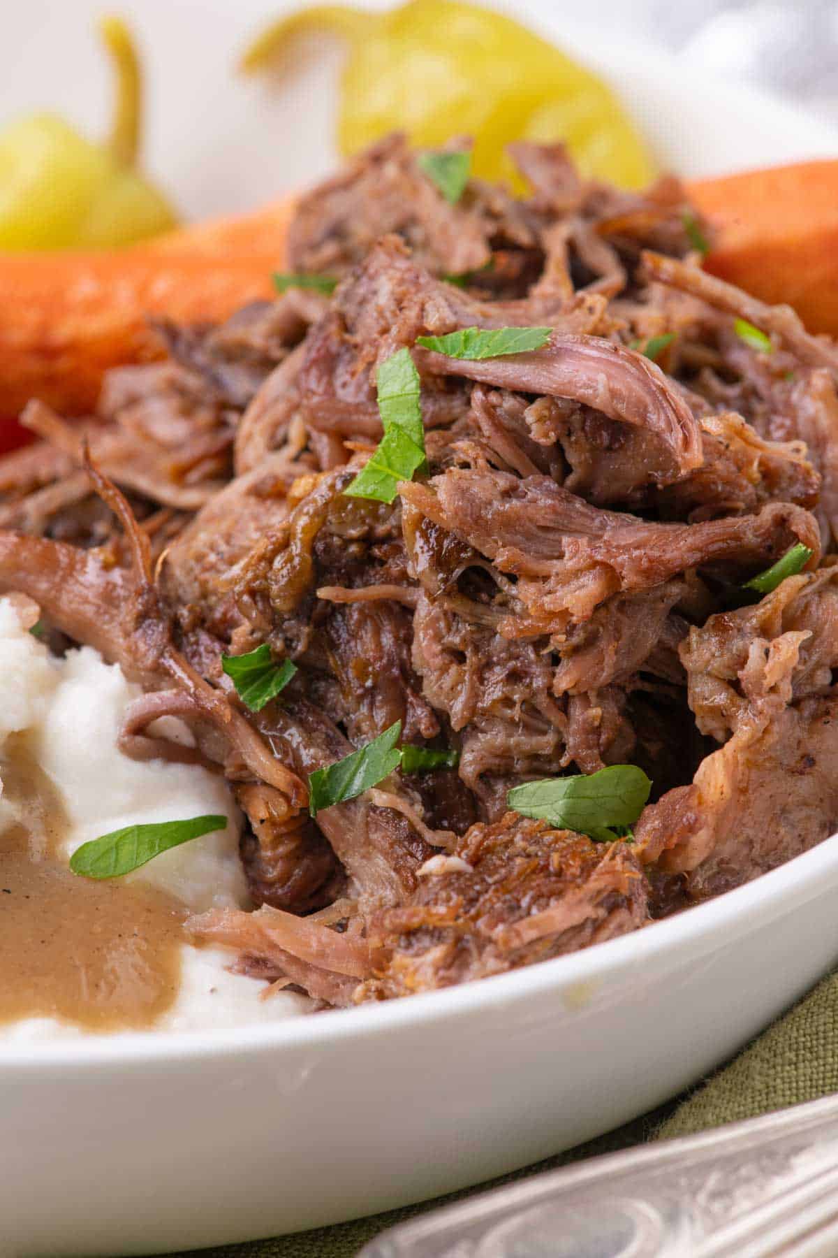 A bowl of shredded mississippi pot roast served with mashed potatoes, gravy, and cooked carrots.