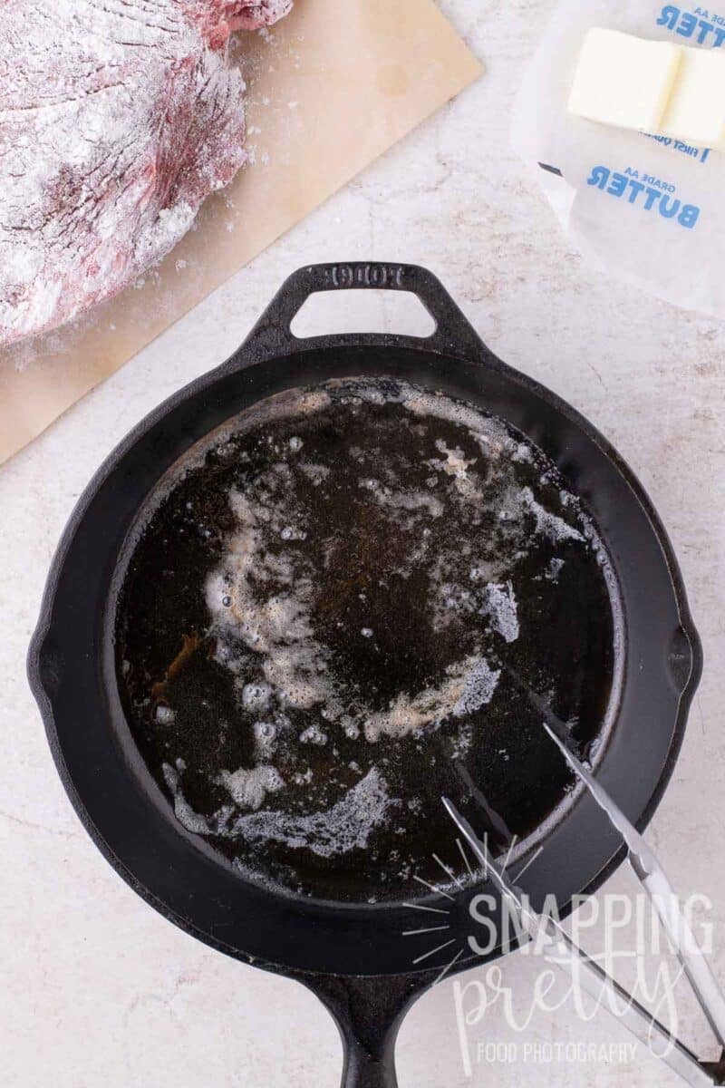 Hot butter bubbling in a cast iron skillet, with a raw roast and butter sticks nearby.