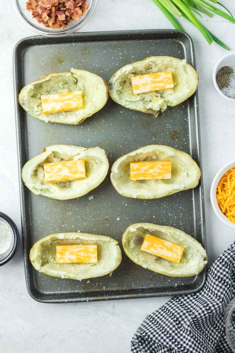 Six hollowed-out potato skins on a baking sheet, each topped with a rectangle of marbled cheese.