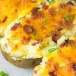 Three twice-baked potatoes topped with melted cheddar cheese, bacon bits, and chopped green onions.