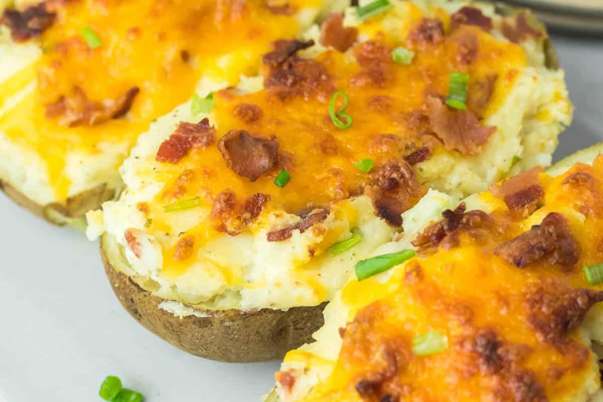 Three twice-baked potatoes topped with melted cheddar cheese, bacon bits, and chopped green onions.