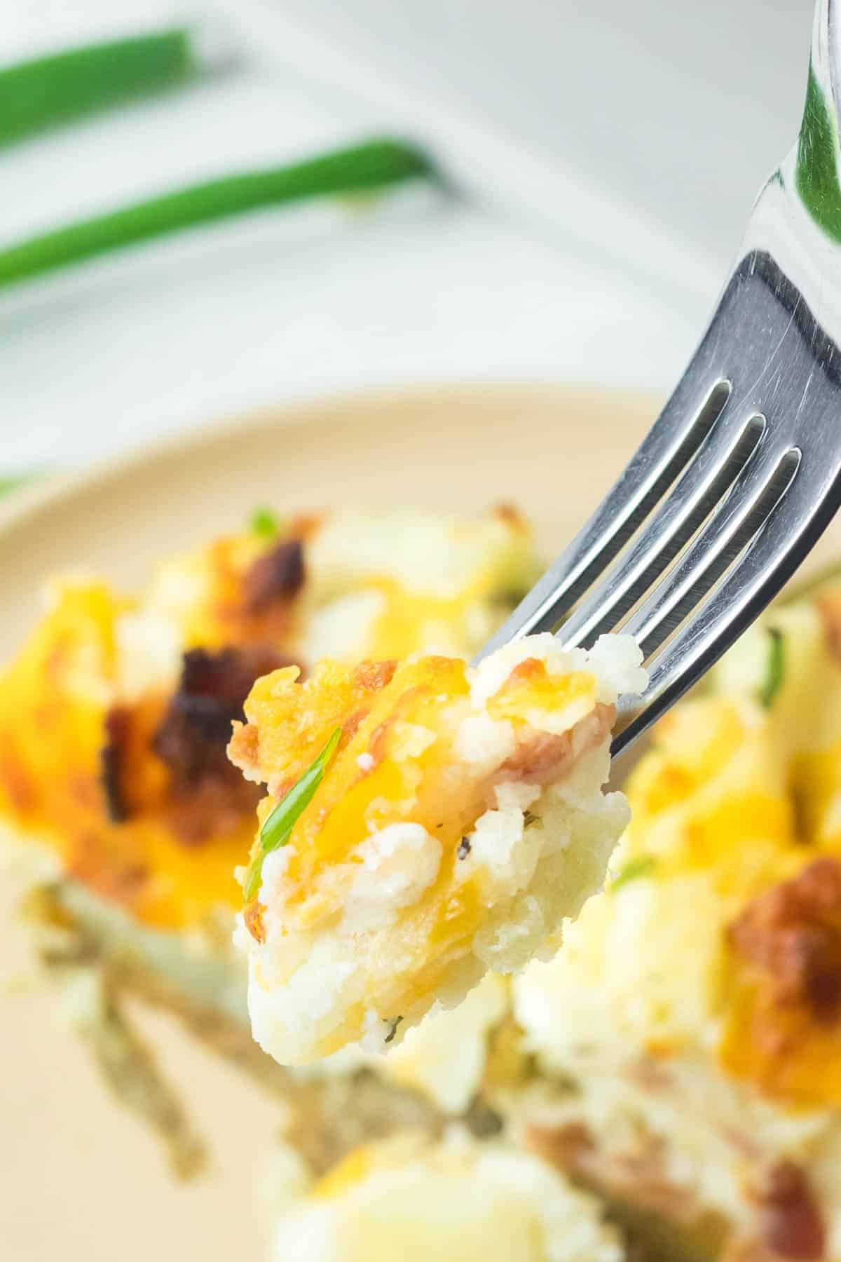 A fork holding a bite of cheesy potato casserole with bacon.