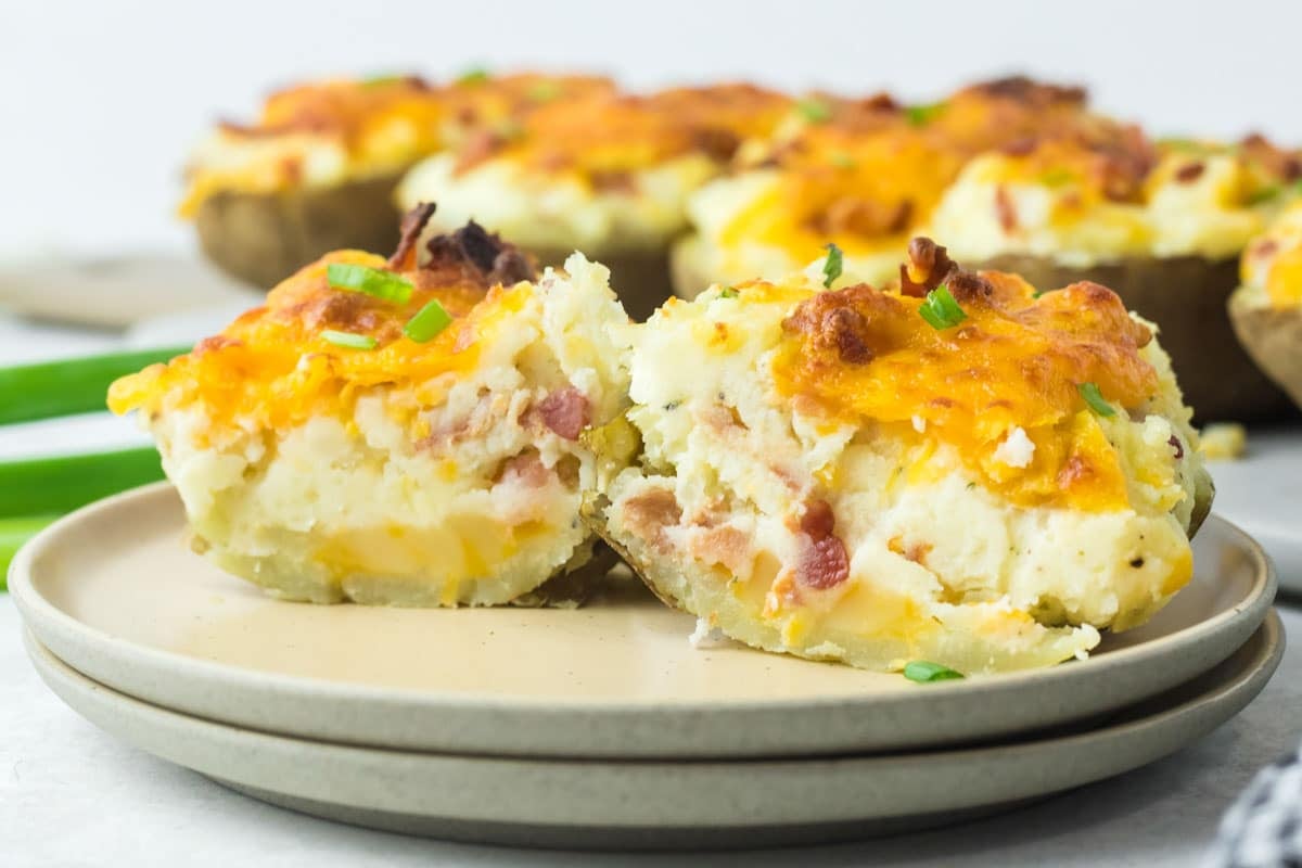 Two halves of a loaded baked potato topped with melted cheddar, bacon, and chives on a plate.